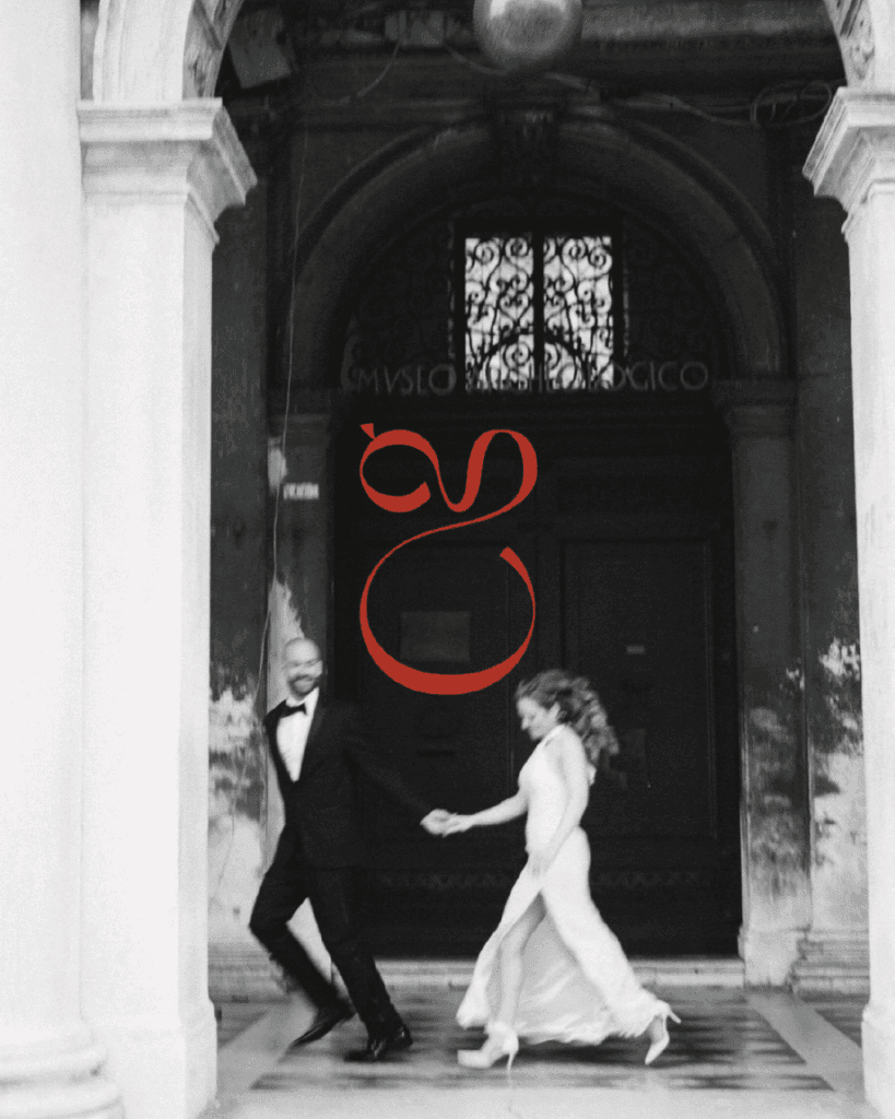 Black and white photo of a couple joyfully walking hand-in-hand under an arched hallway, overlaid with a bold red brand mark.