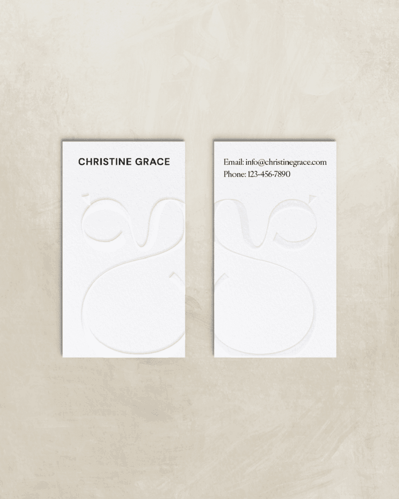 Minimal white business cards embossed with Christine Grace's monogram and contact details, styled on a stone backdrop.