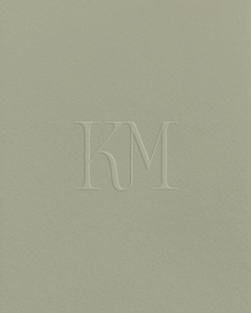 Debossed KM monogram logo for Karen Michelle Photography on textured soft green paper.