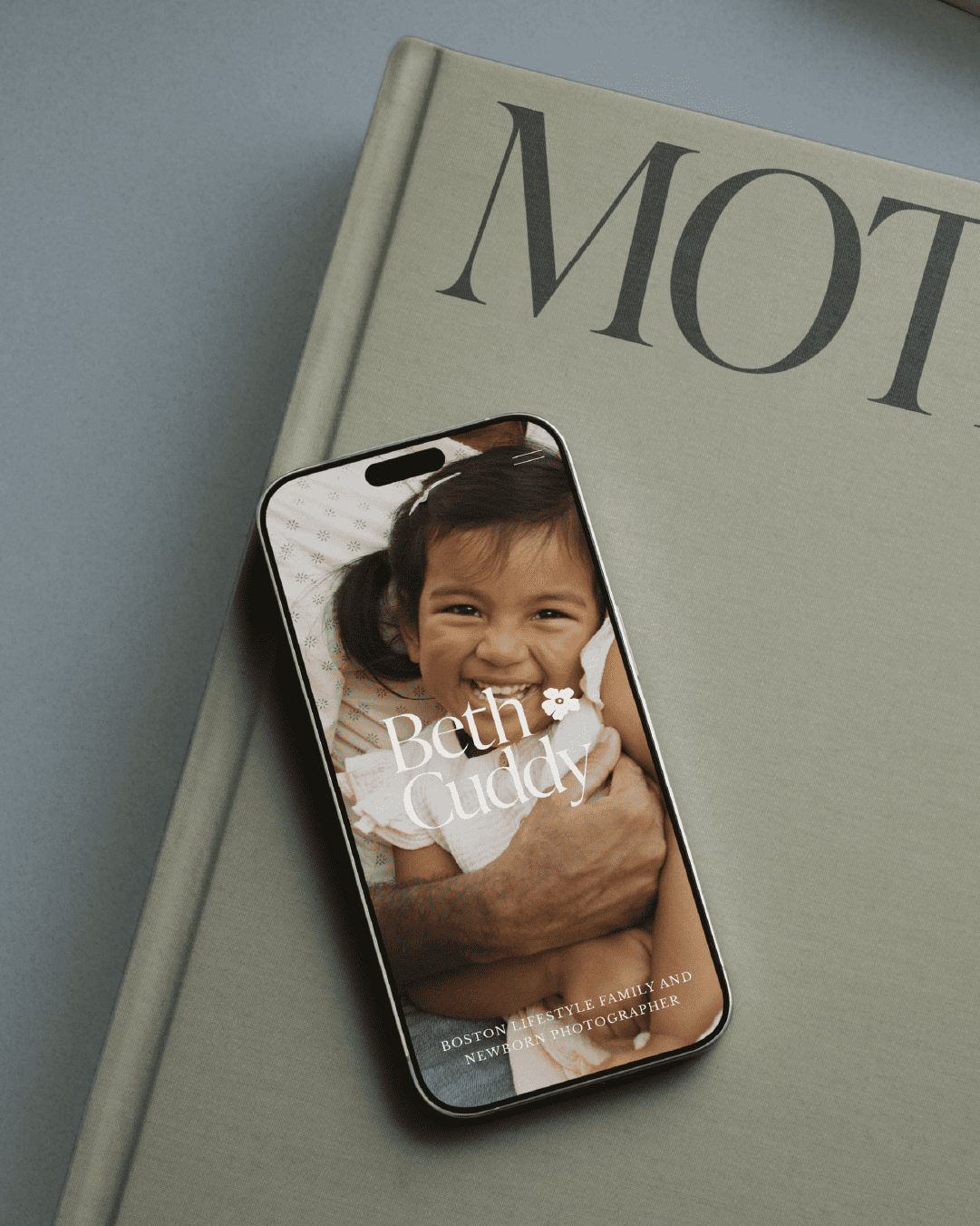 Smartphone mockup showing Beth Cuddy’s brand on screen with a toddler sitting outdoors, and text reading “Boston lifestyle family and newborn photographer.