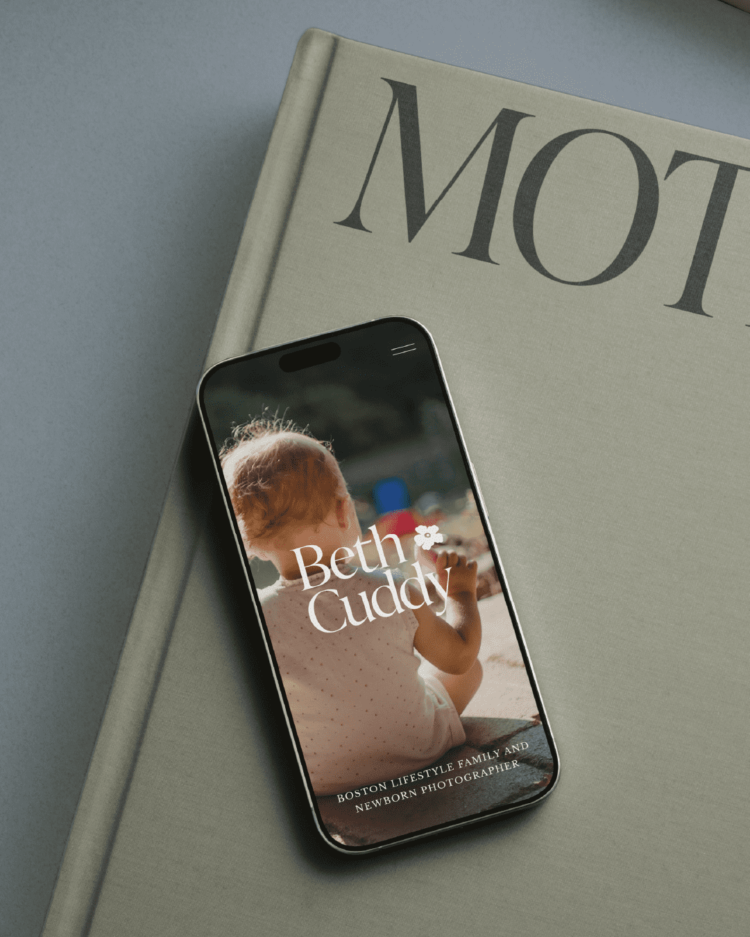 Smartphone mockup showing Beth Cuddy’s brand on screen with a toddler sitting outdoors, and text reading “Boston lifestyle family and newborn photographer.